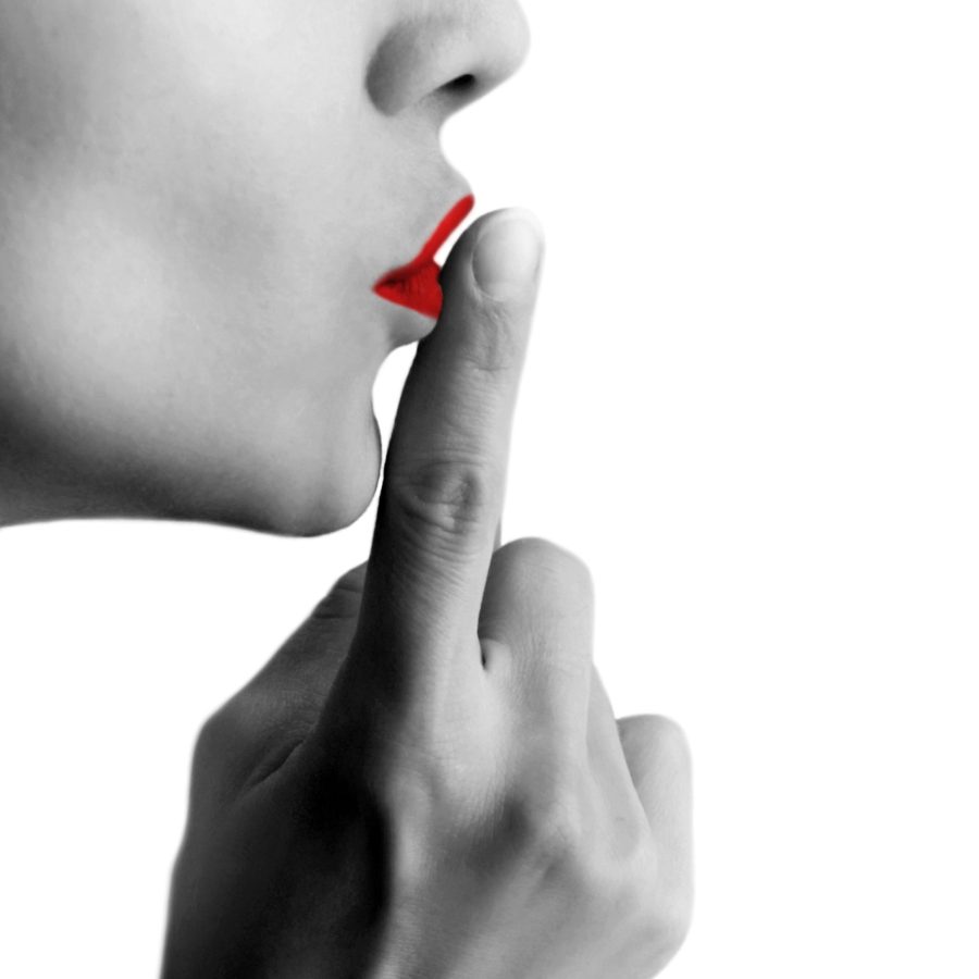 photo d'un visage de femme en profil avec une bouche rouge faisant le geste "chut" avec son doigt